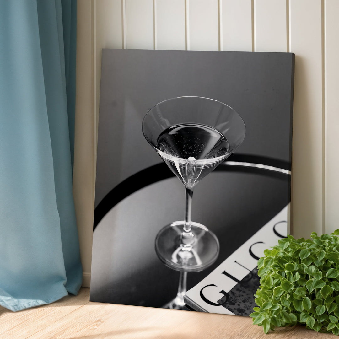 Modern canvas wall art with a black and white photo of a glass on a table and an open magazine in an interior.
