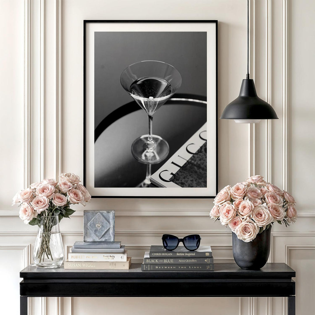 Modern wall art with a black and white photo of a martini glass on a magazine above a console with roses.