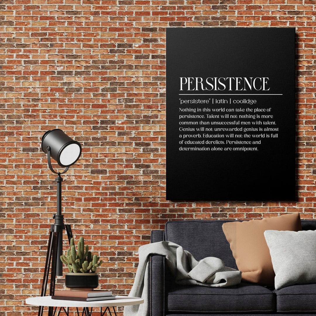 Motivational canvas print with a white quote on a black background above a gray sofa by a brick wall