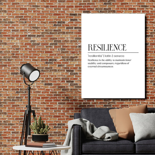 Motivational canvas print with the word Resilience above a dark sofa, industrial lamp and brick wall