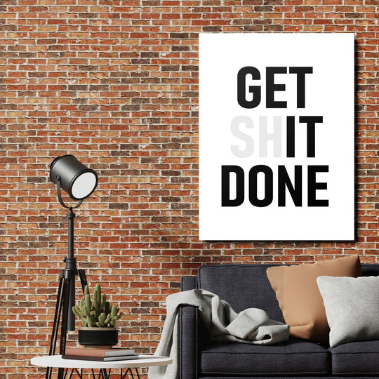 GET SHIT DONE motivational canvas wall art on a brick wall above a sofa in an industrial interior with a lamp and cactus