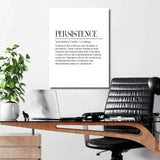Motivational canvas print with a Persistence quote hanging above a desk with a laptop and potted plant in a modern office