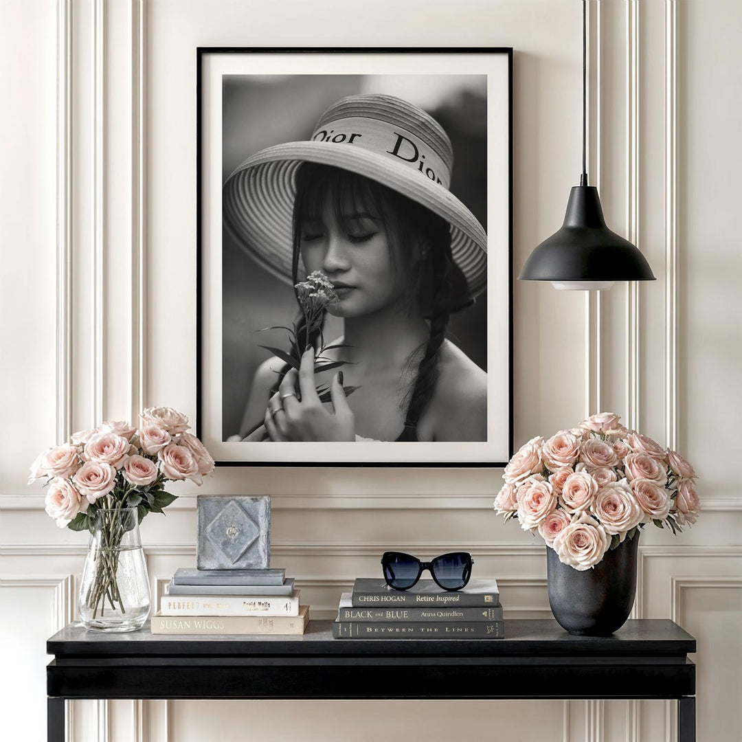 Luxury wall art with a black and white photograph of a woman in a Dior hat smelling a flower