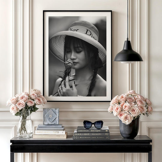 Luxury wall art with a black and white photograph of a woman in a Dior hat smelling a flower