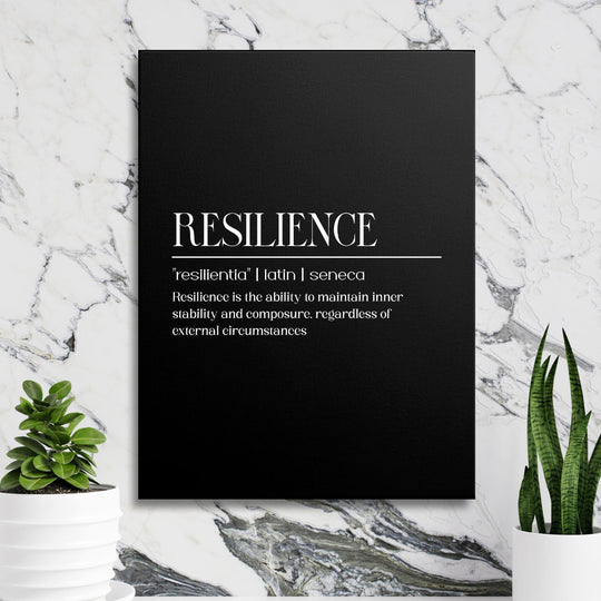 Motivational canvas print with a black-and-white Resilience quote hanging on a marble wall among green plants