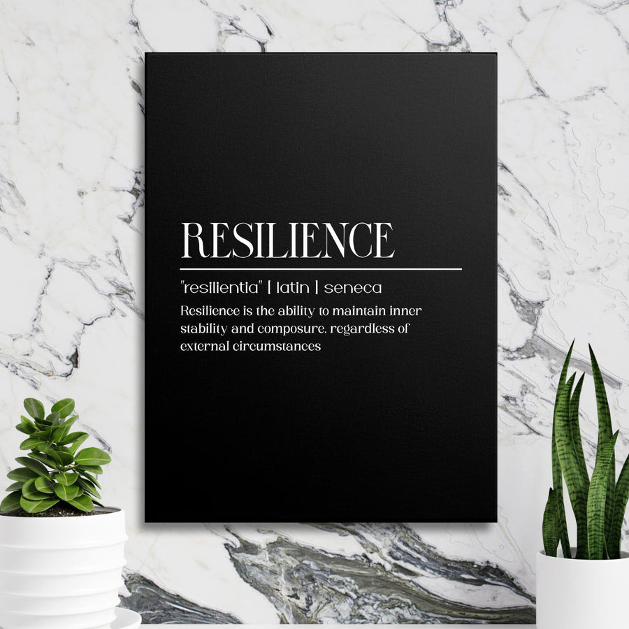 Motivational canvas print with a black-and-white Resilience quote hanging on a marble wall among green plants