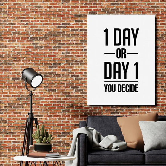 Motivational canvas wall art with the quote “1 DAY OR DAY 1 YOU DECIDE” above a dark gray sofa, lamp and cactus.