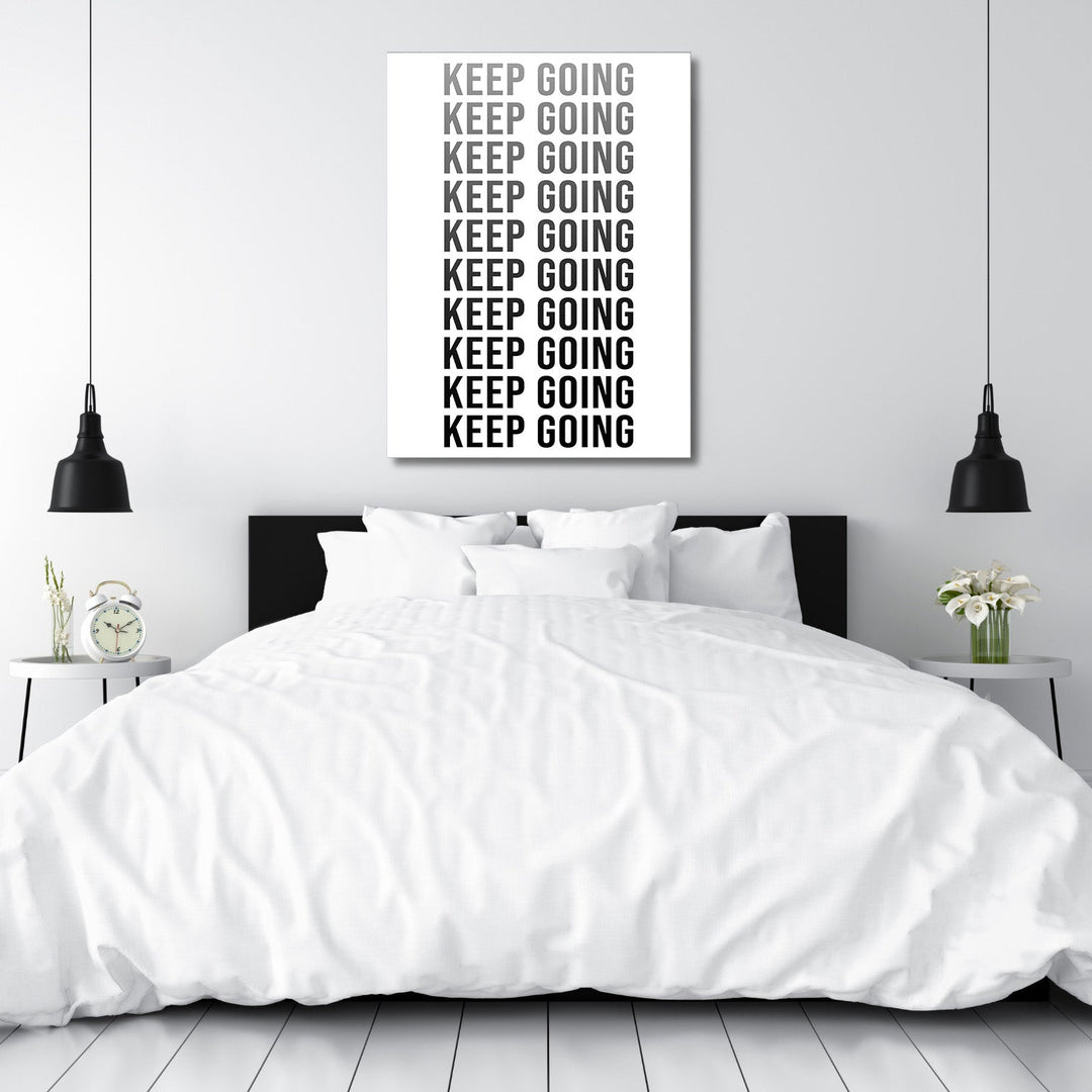 KEEP GOING motivational canvas wall art above a bedroom bed, modern black and white decor in a minimalist interior