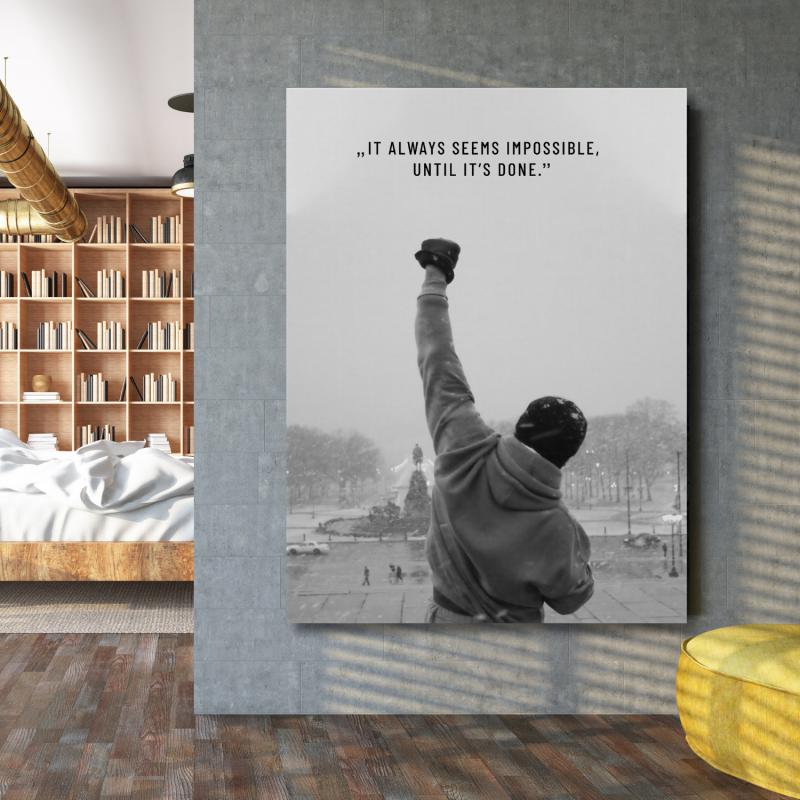 Motivational wall art with the quote “It always seems impossible until it’s done” next to a bookshelf.